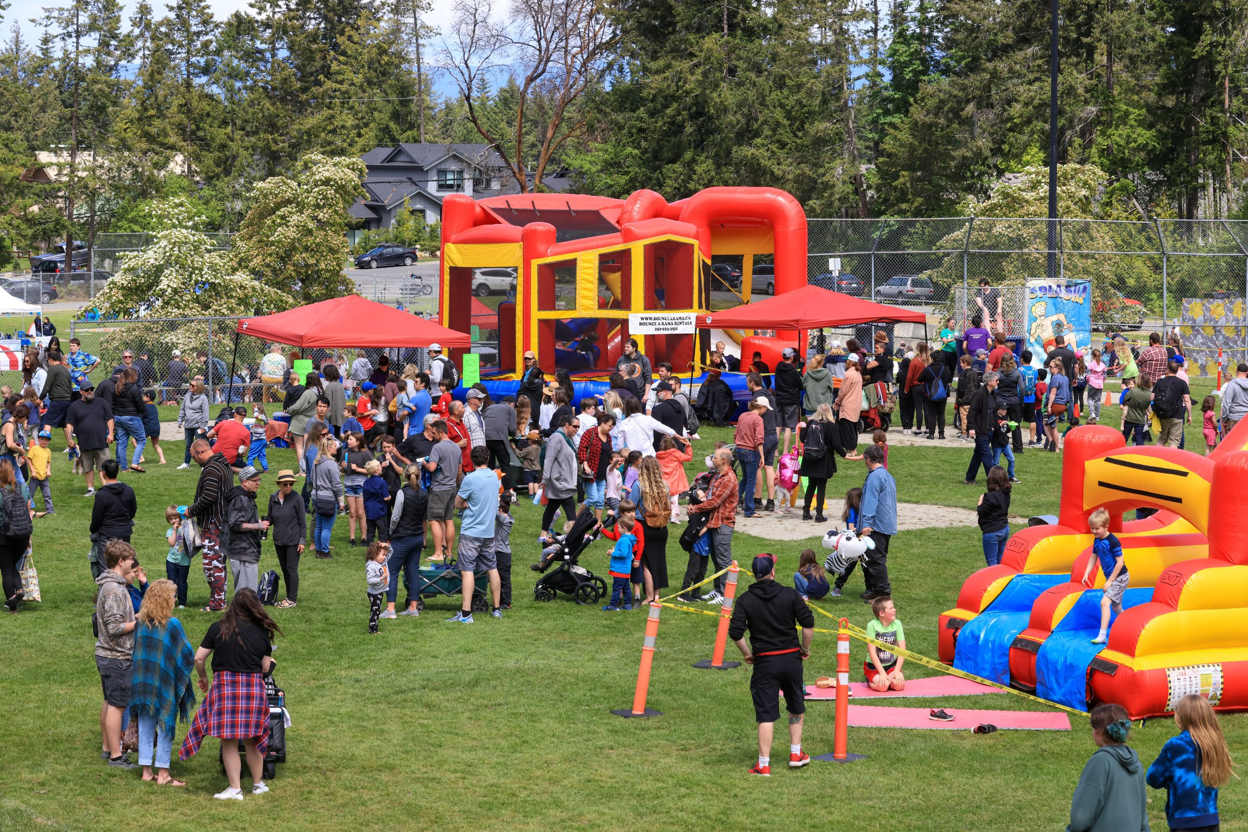 A Family Day Celebration in the park, with families in the park and a bouncy castle.