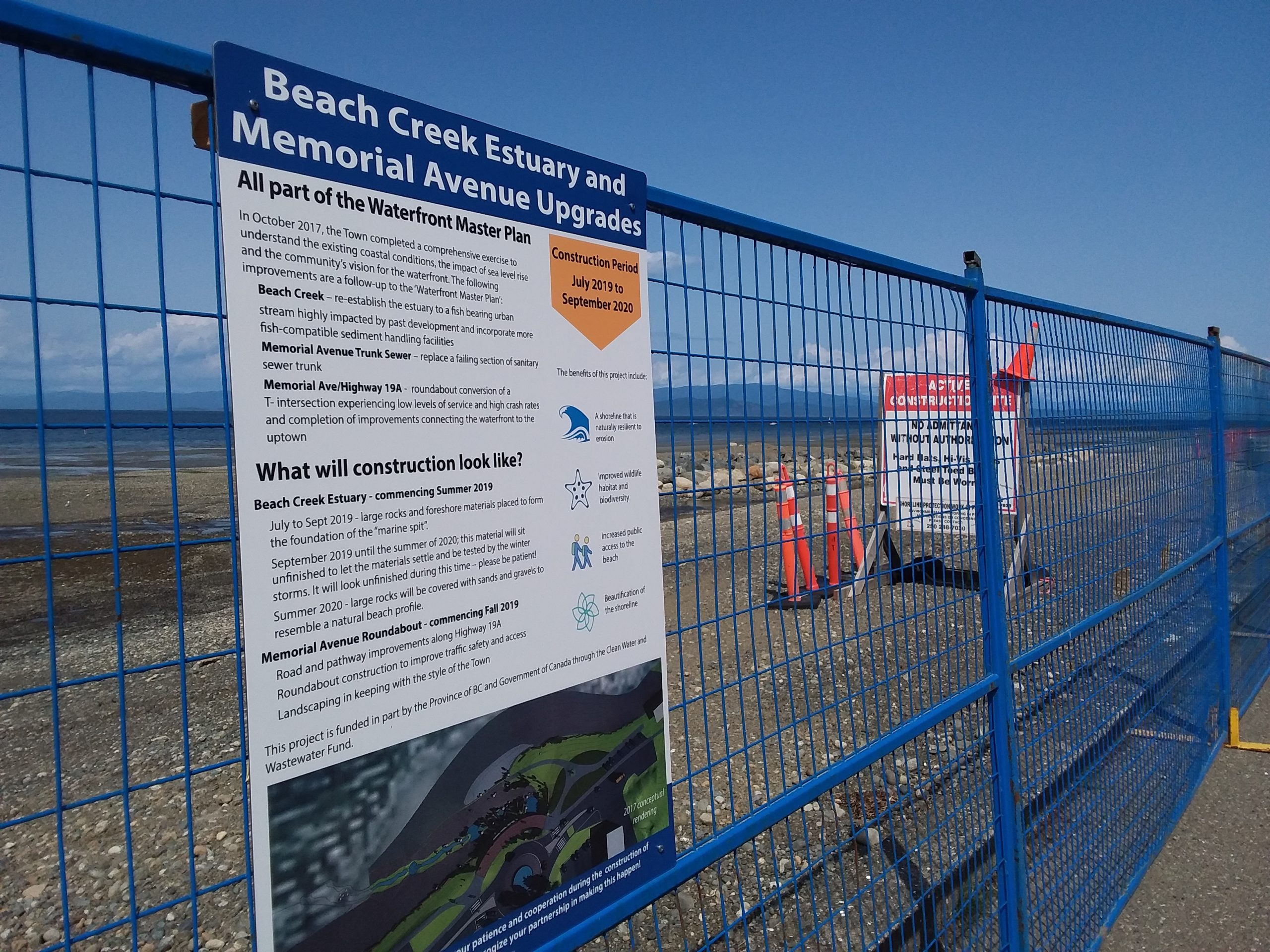 A beach enclosed by a blue gate with a sign that reads 'Beach Creek Estuary and Memorial Avenue Upgrades,' informing the public about the project plans.