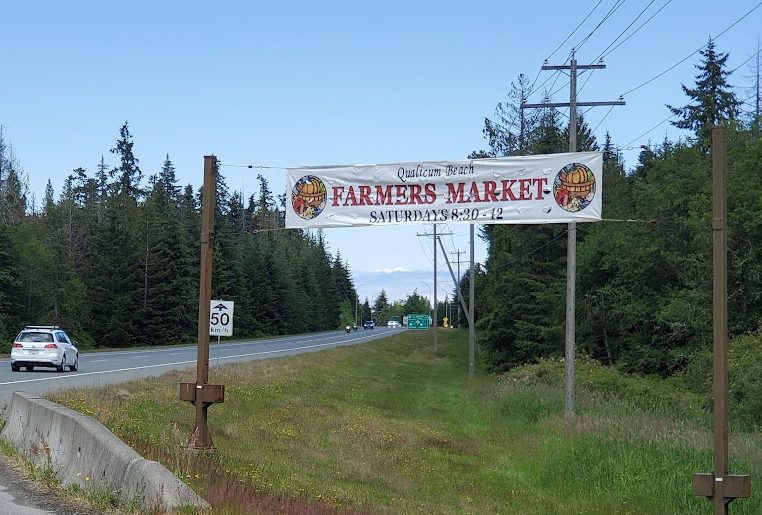 A banner hanging between two telephone poles above a road, with cars driving underneath. The banner reads 