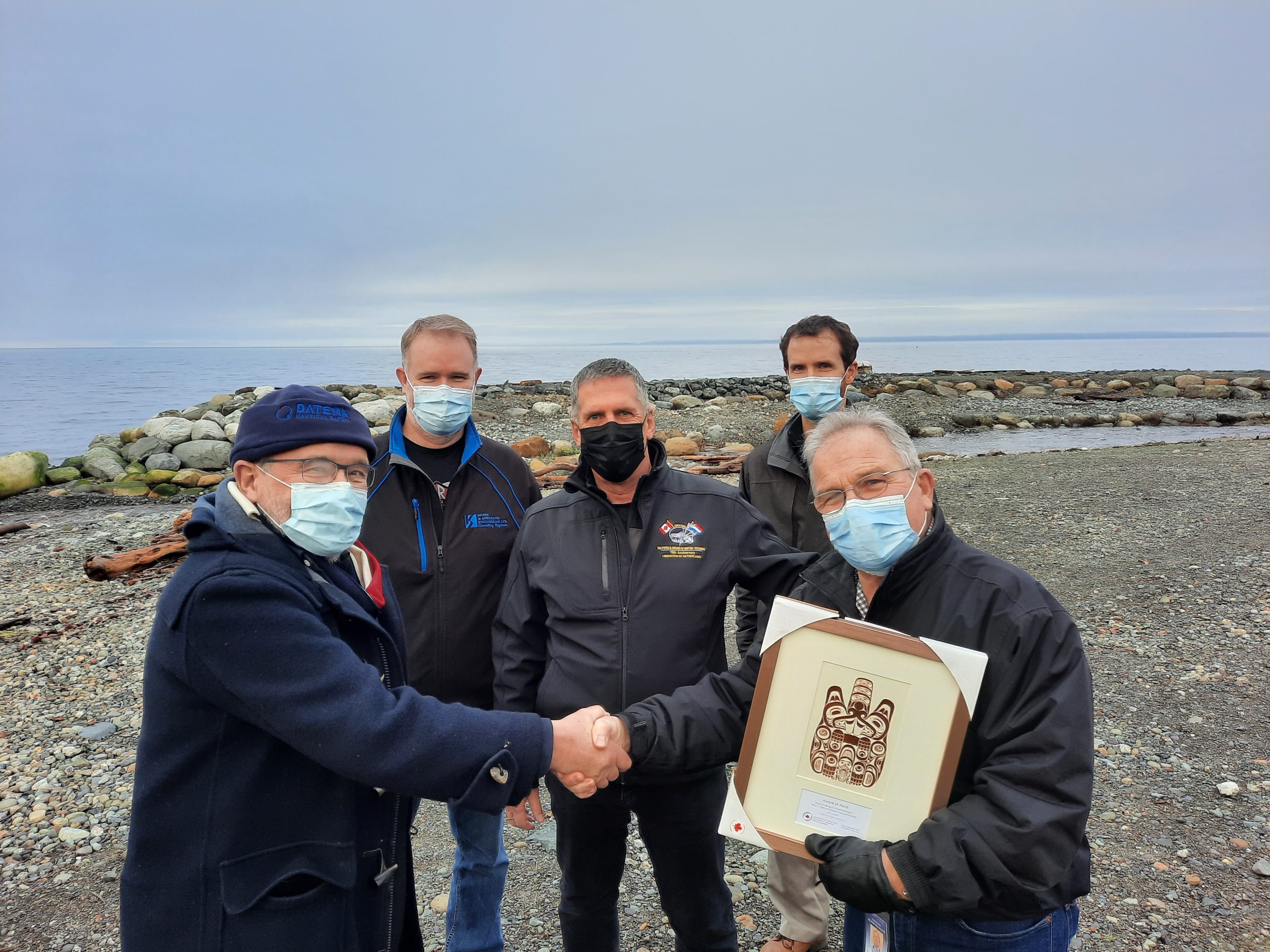 Group of people standing on the beach at the Beach Creek estuary, smiling and holding up an award they won for their project.