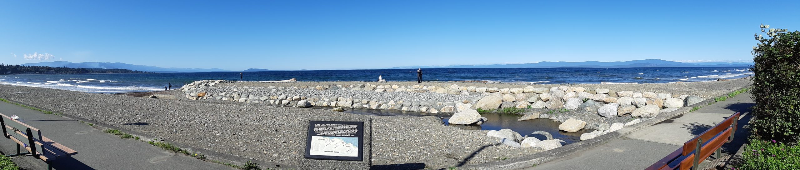 A rocky beach with water in the background and a person standing near the shoreline.