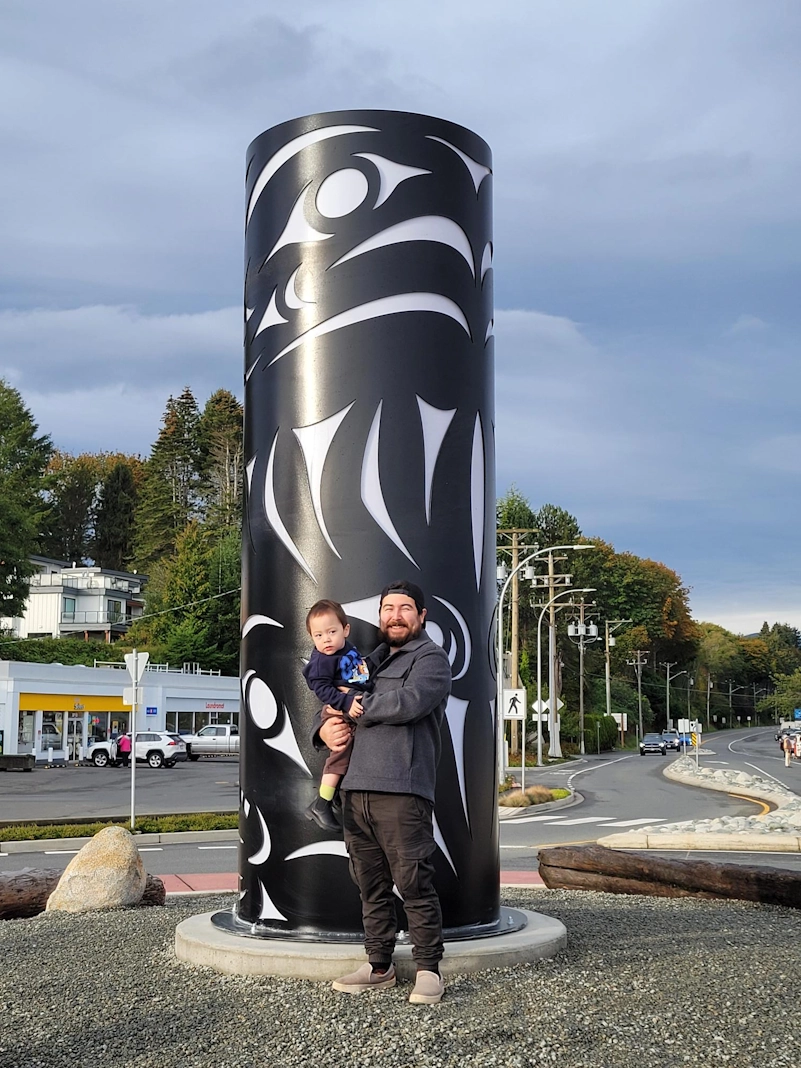 image of Jesse Recalma in front of the artwork he designed for the Memorial Roundabout in Qualicum Beach