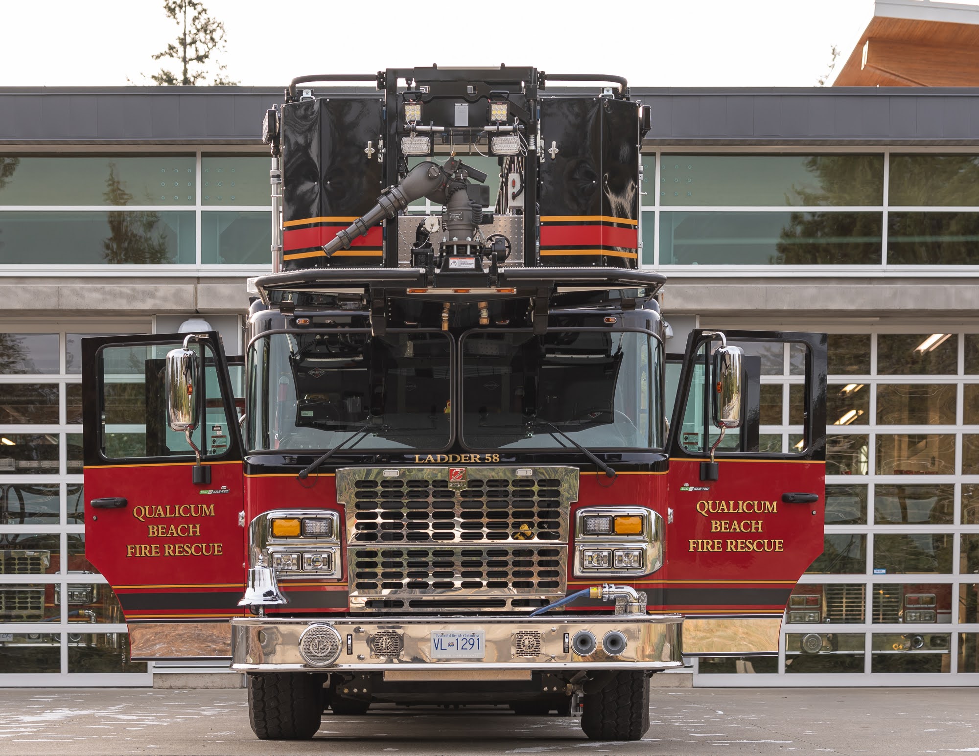 A fire truck parked in front of a fire station with its doors open.