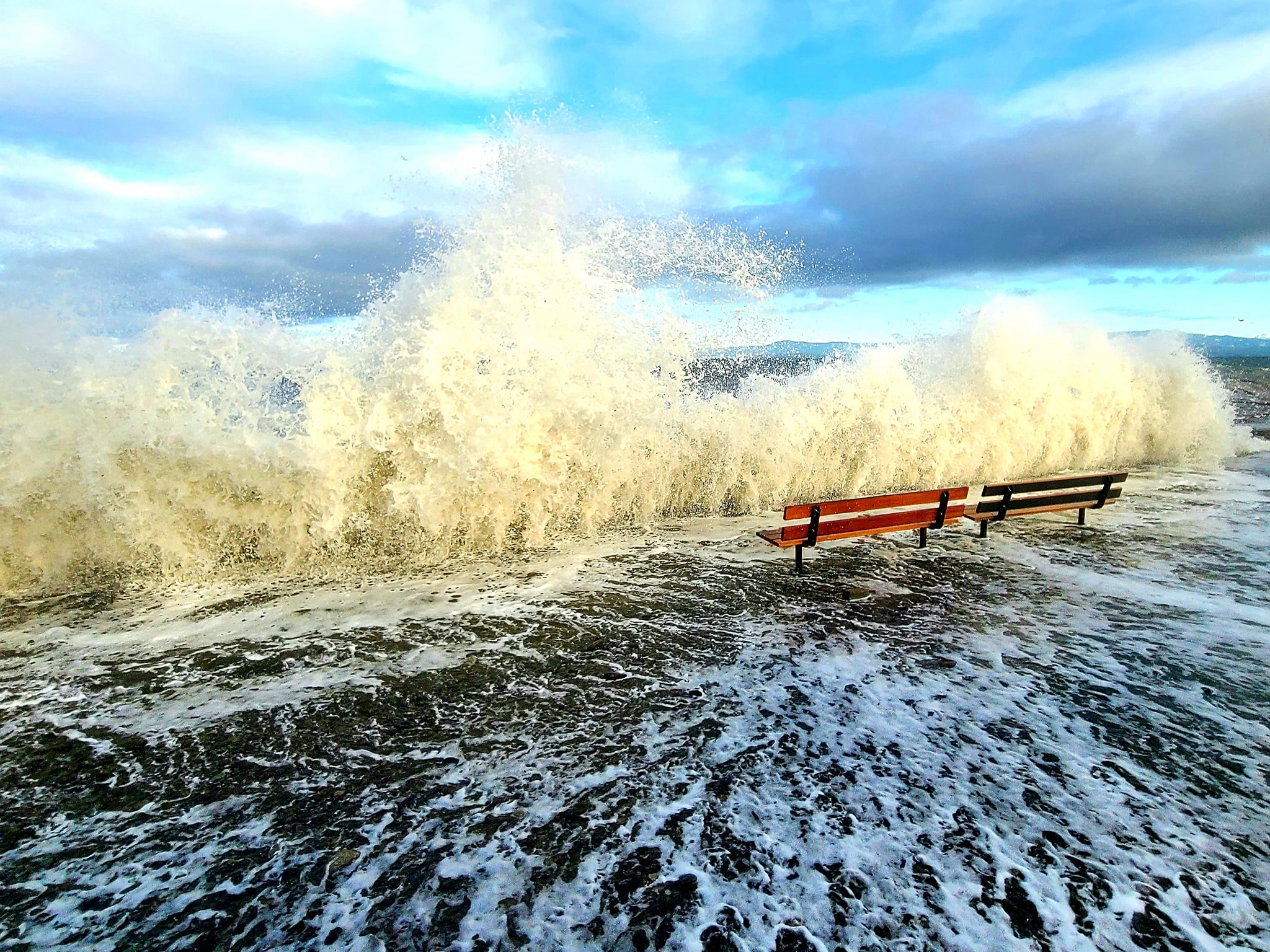 A photos of king tide with high waves crashing against a sea wall.