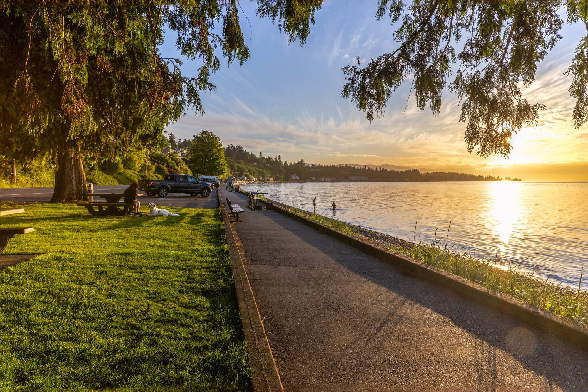 Sunset view of the walkway at Qualicum Beach with people enjoying the evening by the water and a golden sky.