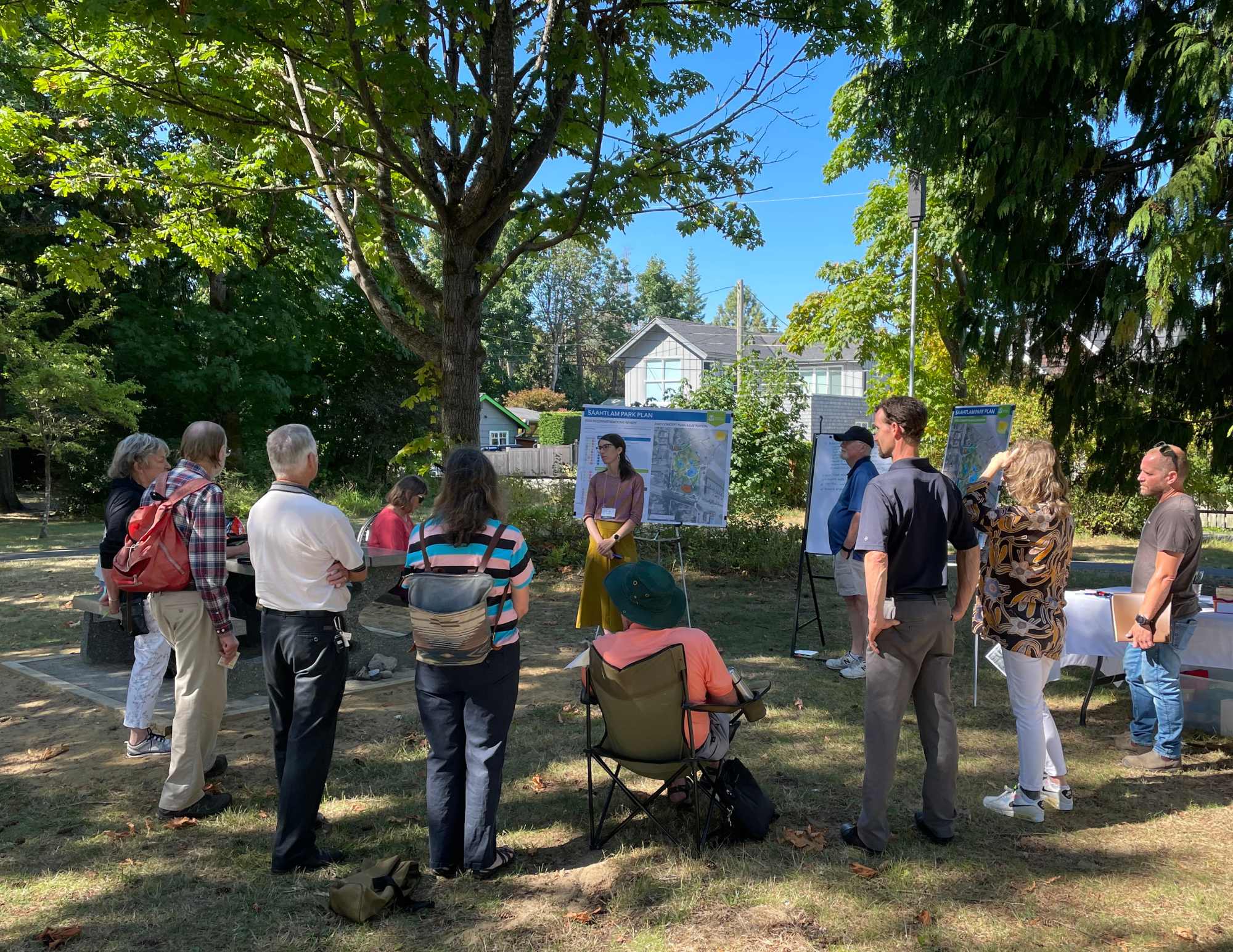 A group of people on the beach in a circle, listening to a government employee presenting a Saahtlam Beach plan on an easel.