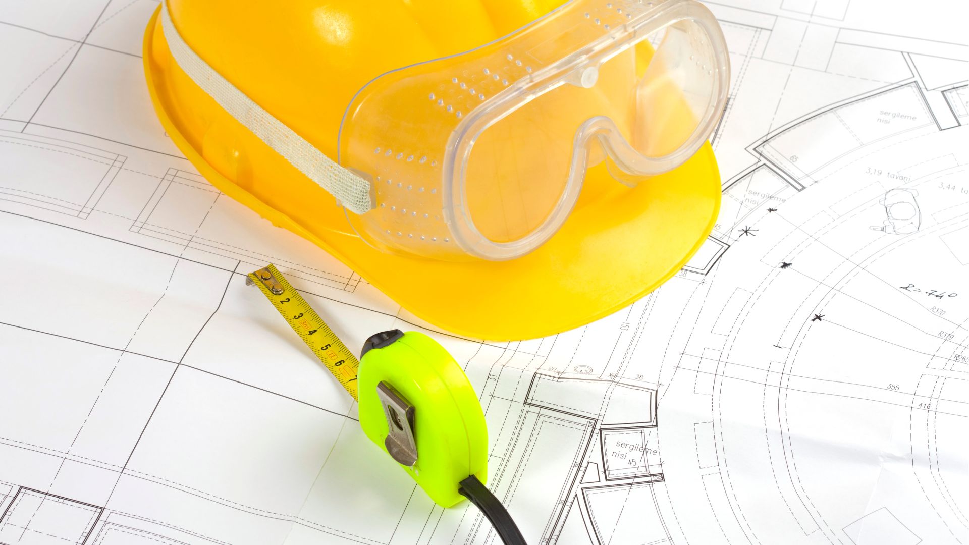 A hardhat and measuring tape on top of architectural building plans