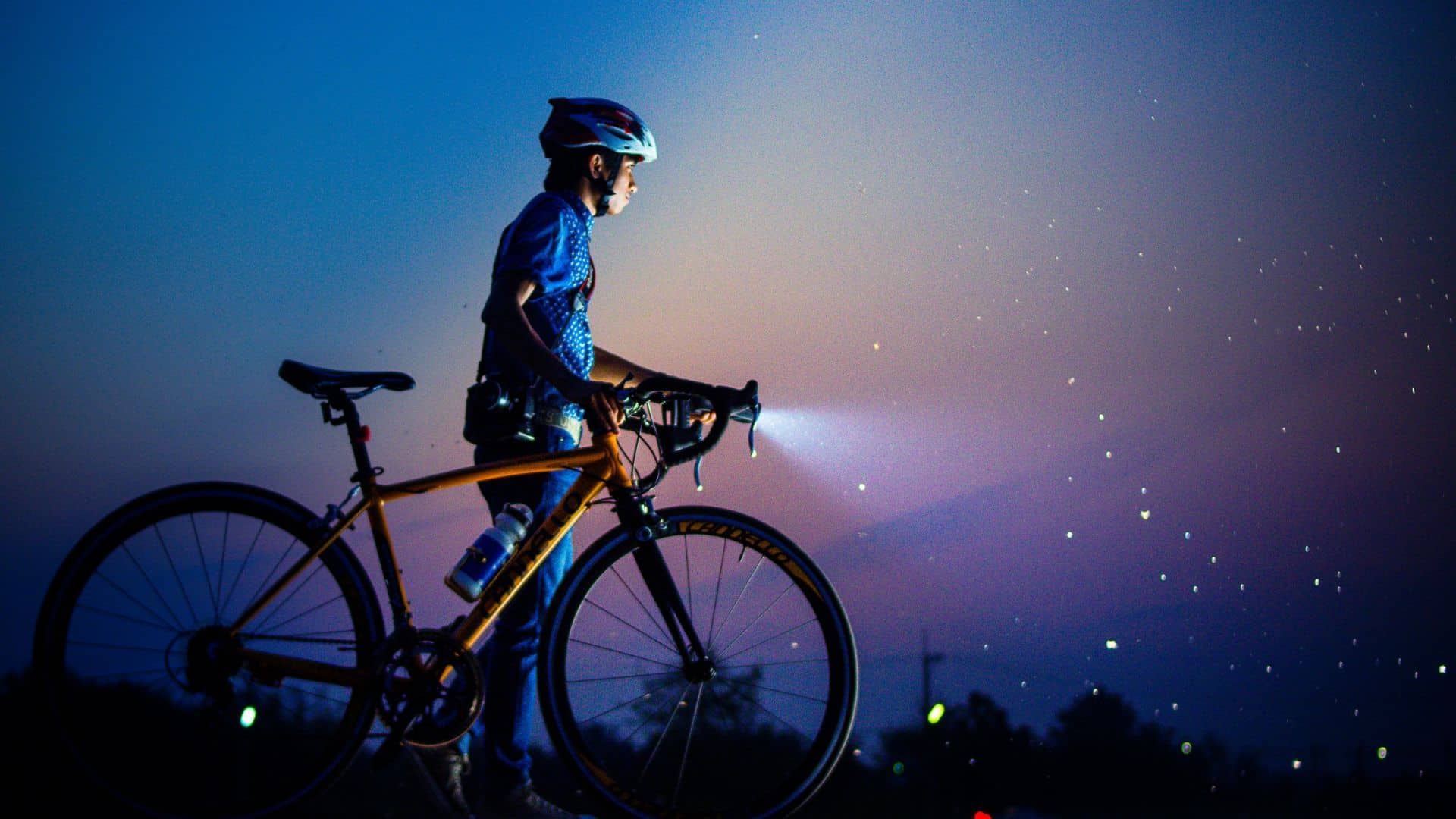 A mountain bike with a cyclist shining a light on the front of the bike, highlighting Cycling Safety.