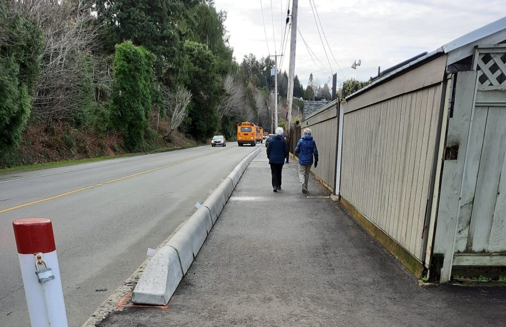 Photo of the Waterfront Walkway, with two people walking, a road on one side, and a fence on the other.