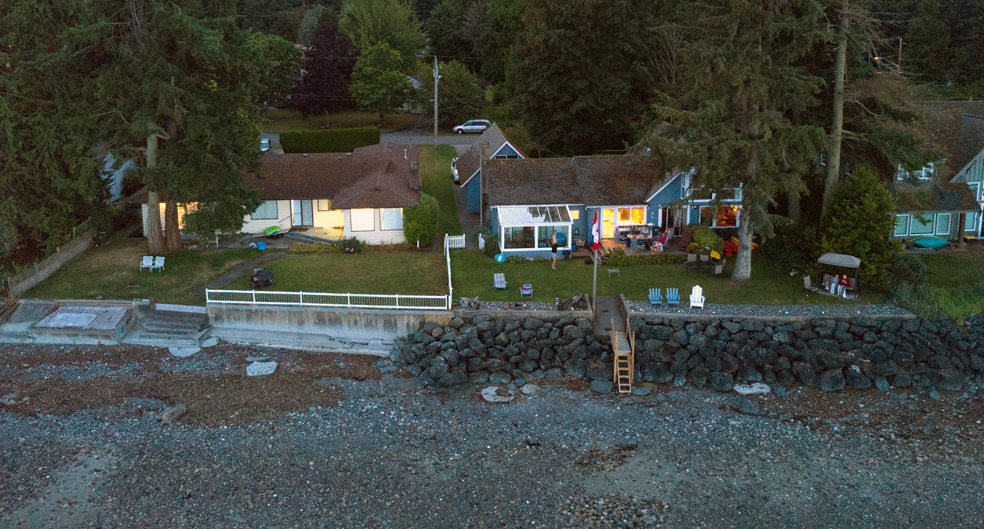 Two houses with a forest backdrop, a rocky beach in front, and pathways leading down to the shore.