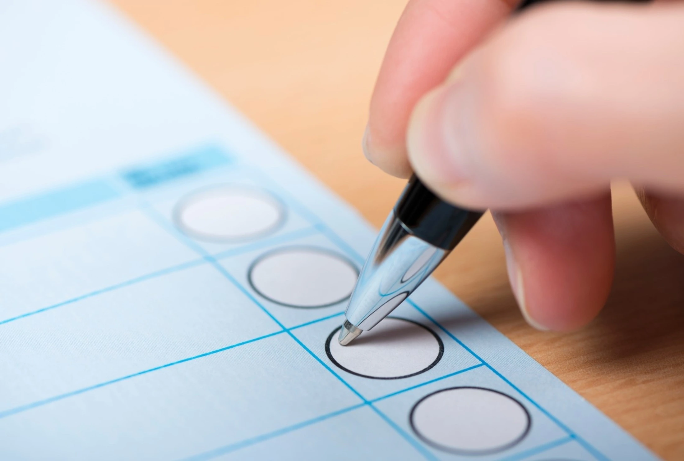 A person writes on a blue election ballet with a ball point pen.