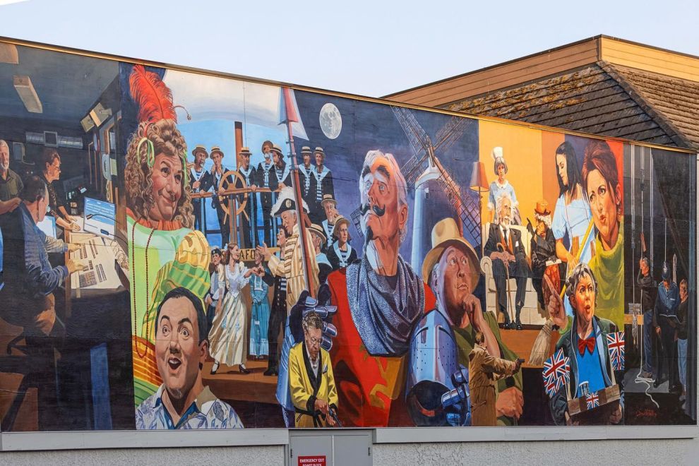 A mural painted on the exterior wall of a building, featuring various people depicted in vibrant colors.