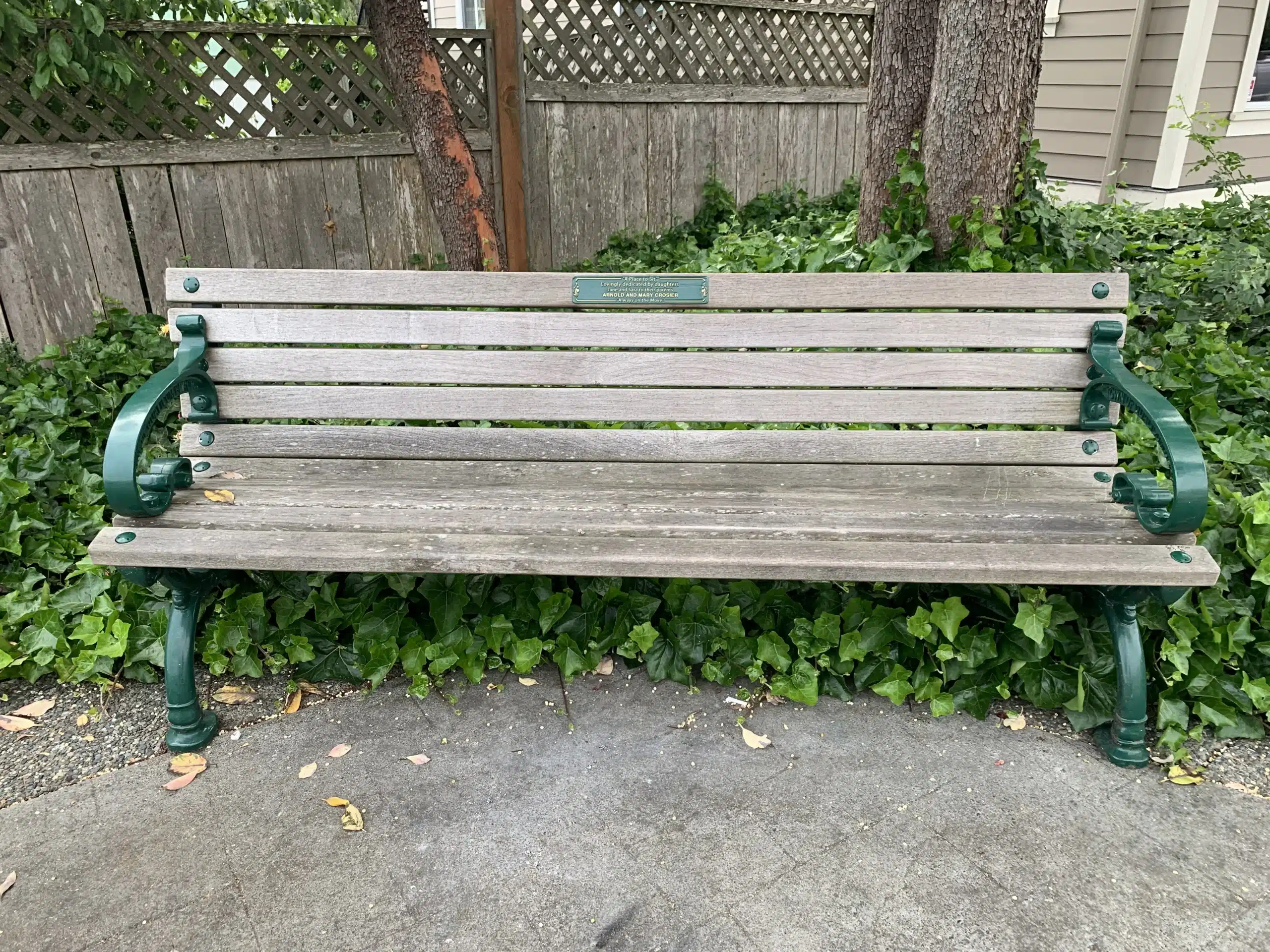 Wooden bench with green handles, and a dedication plaque at the top of the backrest.