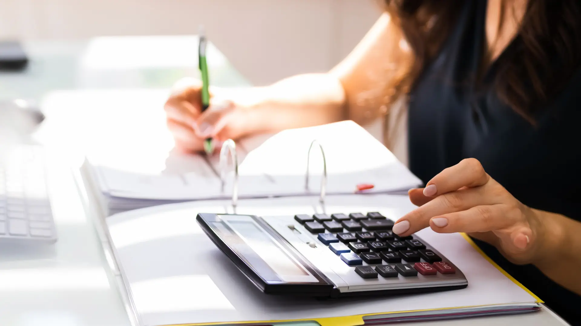 Person writing in a notebook and using a calculator.