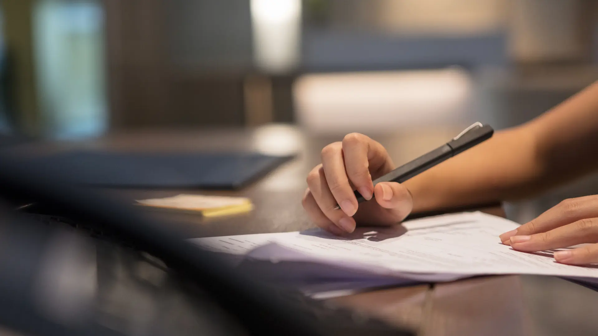 Person completing paperwork at a desk, only hands pictured.