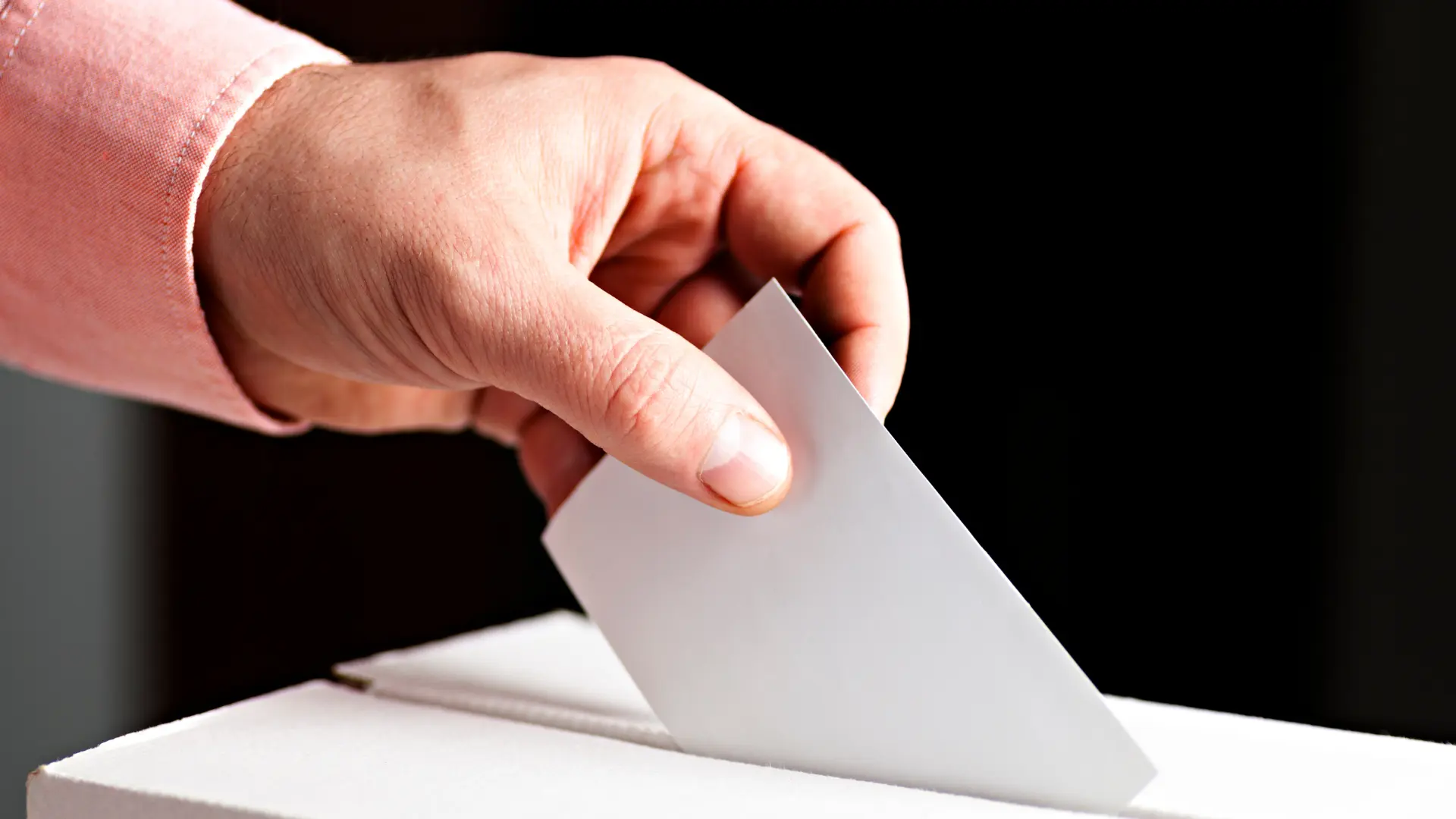 Person putting a ballot into a white ballot box.